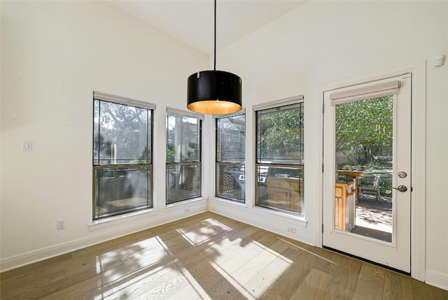 unfurnished dining area with wood-type flooring and high vaulted ceiling