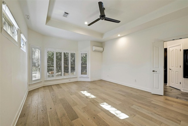 empty room featuring light hardwood / wood-style flooring, a raised ceiling, ceiling fan, and a wall unit AC