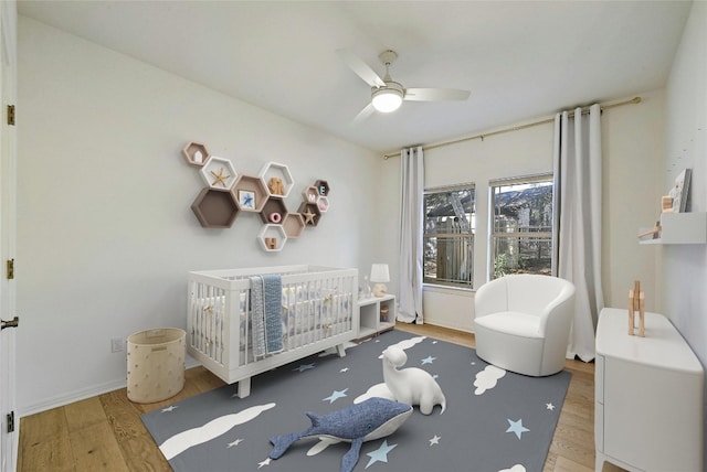 bedroom featuring hardwood / wood-style flooring, ceiling fan, and a nursery area