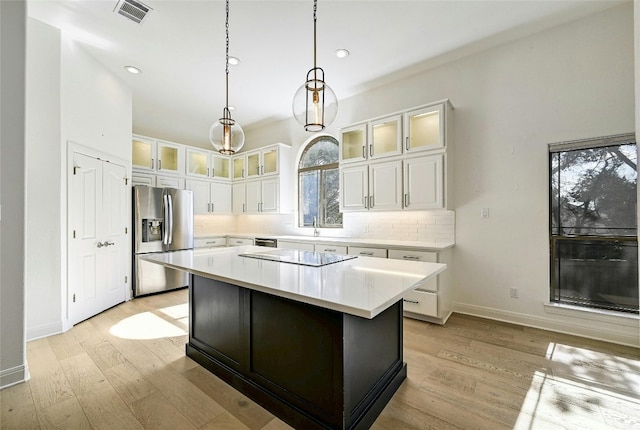 kitchen with hanging light fixtures, stainless steel appliances, a kitchen island, white cabinets, and light wood-type flooring