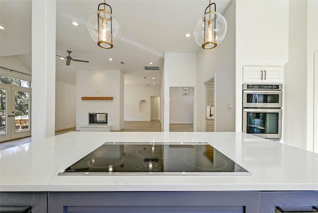 kitchen with french doors, light stone countertops, black electric cooktop, double oven, and decorative light fixtures