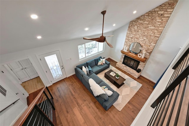 living room with dark hardwood / wood-style floors, a stone fireplace, ceiling fan, and lofted ceiling