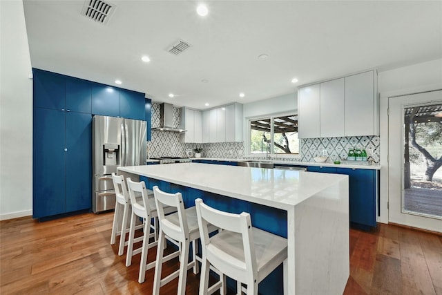 kitchen featuring appliances with stainless steel finishes, light wood-type flooring, wall chimney exhaust hood, white cabinets, and a center island