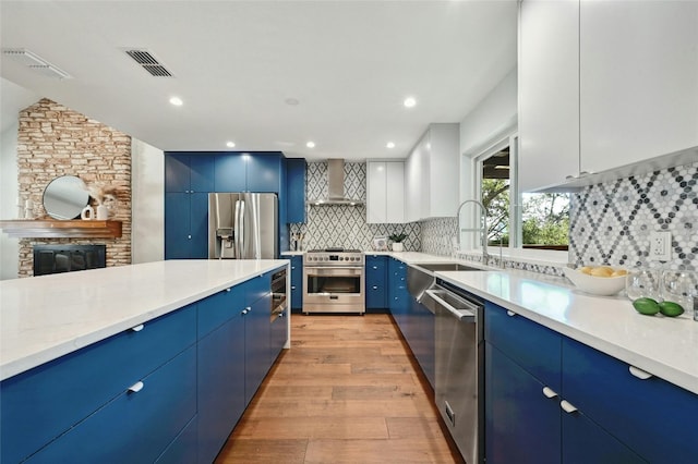 13016 S Madrone Trl, Austin, TX 78737 - kitchen featuring stainless steel appliances, blue cabinetry, wall chimney exhaust hood, light wood-style floors, and backsplash