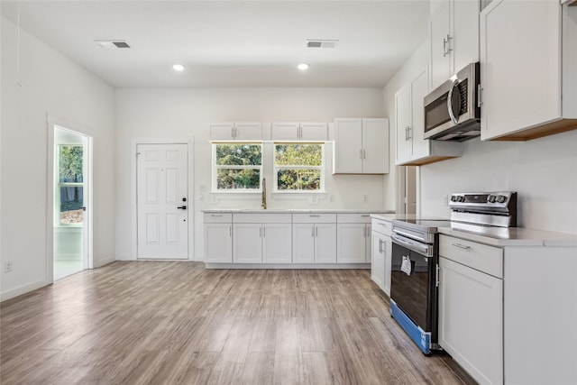 kitchen featuring white cabinets, appliances with stainless steel finishes, light hardwood / wood-style floors, and sink