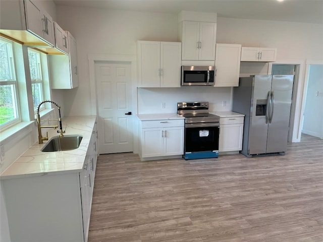 kitchen featuring light stone countertops, sink, stainless steel appliances, light hardwood / wood-style floors, and white cabinets