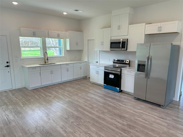 kitchen with sink, white cabinets, light wood-type flooring, and appliances with stainless steel finishes