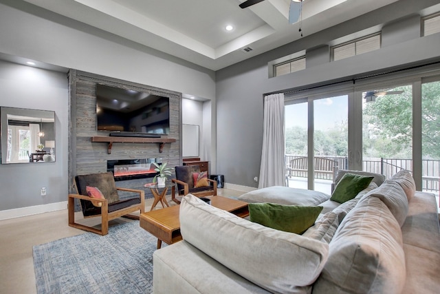 living room with ceiling fan, a large fireplace, and a tray ceiling