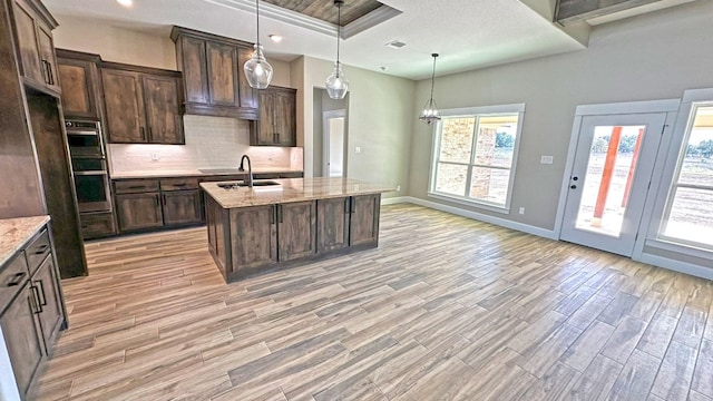 kitchen with light stone countertops, a kitchen island with sink, pendant lighting, and light hardwood / wood-style floors