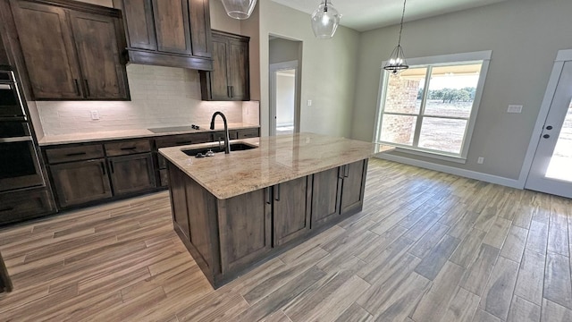 kitchen featuring light hardwood / wood-style flooring, a center island with sink, oven, and light stone counters