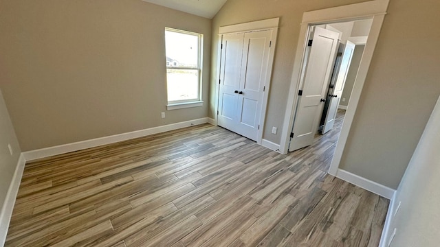 unfurnished bedroom featuring vaulted ceiling, light wood-type flooring, and a closet