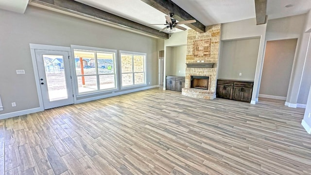 unfurnished living room featuring beam ceiling, light hardwood / wood-style floors, a stone fireplace, and ceiling fan