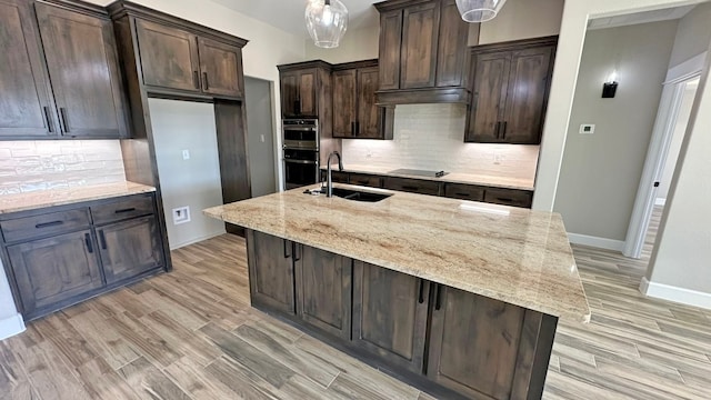 kitchen featuring light stone countertops, an island with sink, tasteful backsplash, and sink