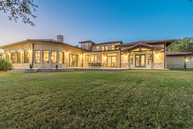 back house at dusk with french doors and a lawn