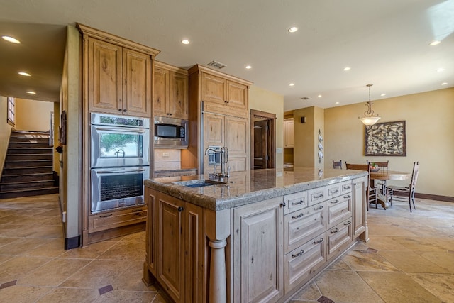 kitchen featuring sink, built in appliances, an island with sink, decorative light fixtures, and light stone counters