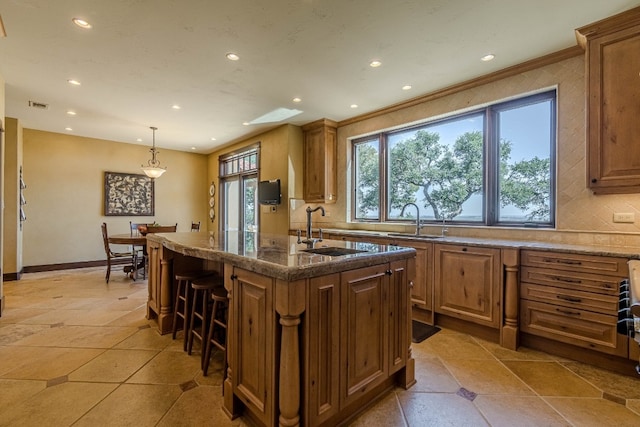 kitchen with a breakfast bar, a kitchen island with sink, sink, and pendant lighting