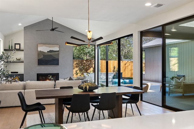 dining space with a fireplace, light hardwood / wood-style floors, vaulted ceiling, and plenty of natural light