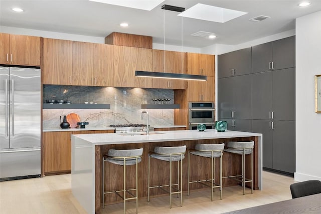 2606 Cavileer Ave, Austin, TX 78757 - kitchen with appliances with stainless steel finishes, a skylight, light wood-style flooring, backsplash, and a kitchen breakfast bar