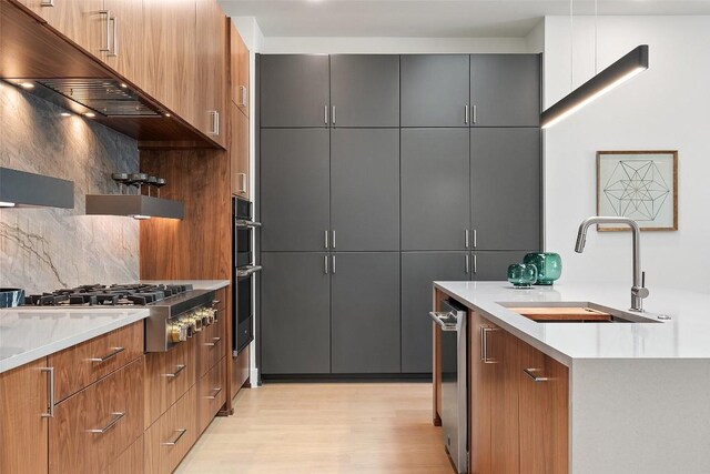 2606 Cavileer Ave, Austin, TX 78757 - kitchen featuring under cabinet range hood, modern cabinets, light wood finished floors, backsplash, and appliances with stainless steel finishes