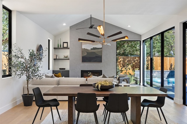 dining area featuring a healthy amount of sunlight, lofted ceiling, a fireplace, and light hardwood / wood-style flooring