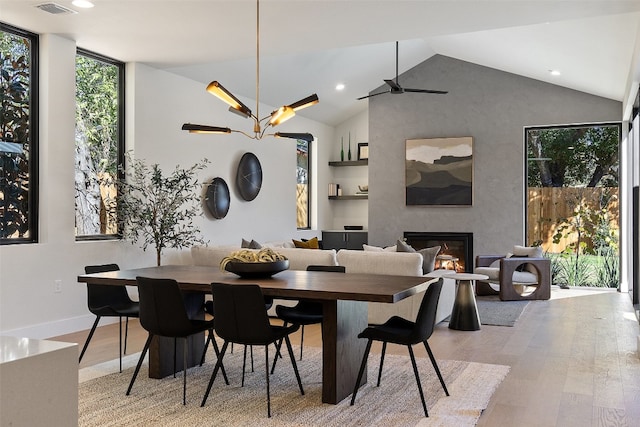 dining area with a large fireplace, ceiling fan with notable chandelier, lofted ceiling, and light wood-type flooring