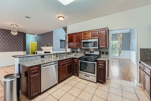 kitchen featuring kitchen peninsula, stainless steel appliances, stone counters, and sink