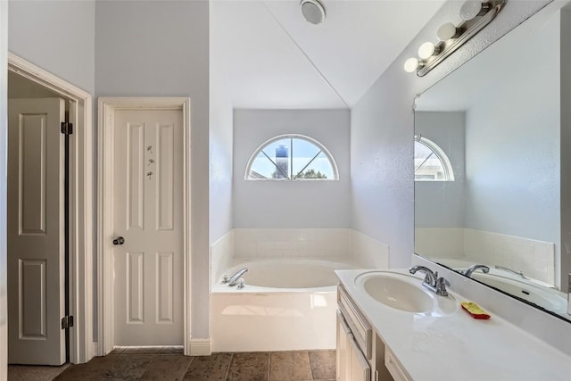 bathroom with lofted ceiling, vanity, tiled bath, and a healthy amount of sunlight