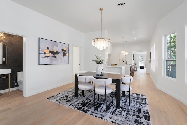 dining area with an inviting chandelier, sink, and light wood-type flooring