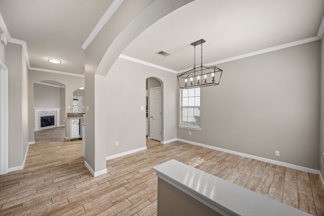 unfurnished dining area featuring a stone fireplace, ornamental molding, a notable chandelier, and light wood-type flooring