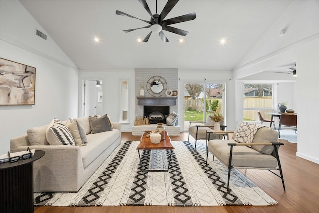 living room with light wood finished floors, visible vents, ceiling fan, a fireplace, and high vaulted ceiling