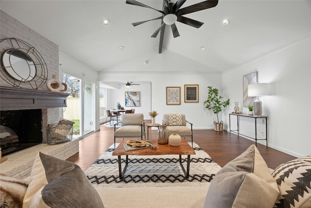 living room featuring vaulted ceiling with beams, a brick fireplace, wood finished floors, and a ceiling fan