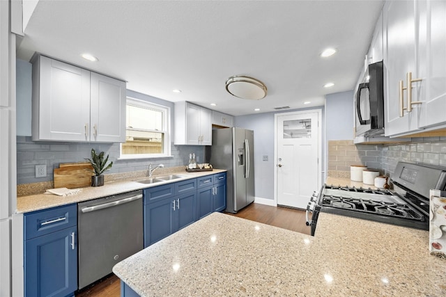 kitchen with appliances with stainless steel finishes, light stone counters, blue cabinets, white cabinetry, and a sink