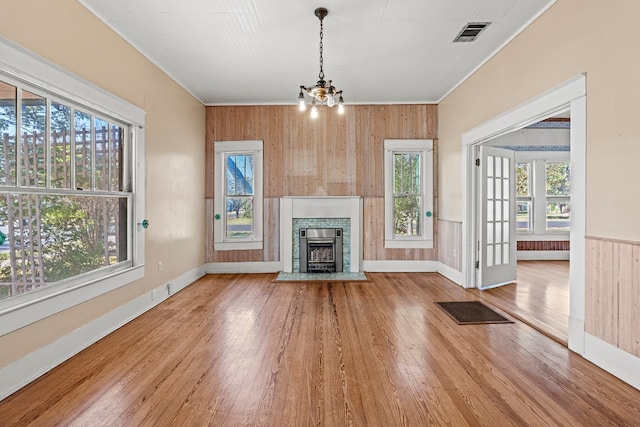 unfurnished living room featuring wood walls, plenty of natural light, wood-type flooring, and a notable chandelier