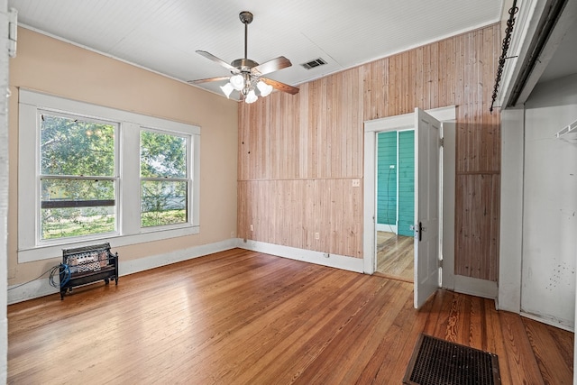 empty room with wooden walls, ceiling fan, and light hardwood / wood-style floors