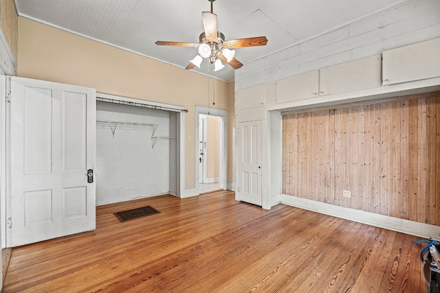 unfurnished bedroom with light hardwood / wood-style floors, ceiling fan, and wood walls