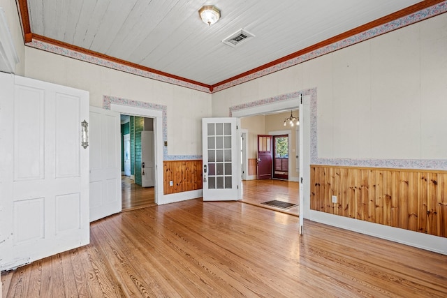 empty room featuring wood walls, wooden ceiling, light wood-type flooring, ornamental molding, and a notable chandelier