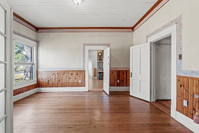 empty room featuring wood-type flooring, crown molding, and wooden walls