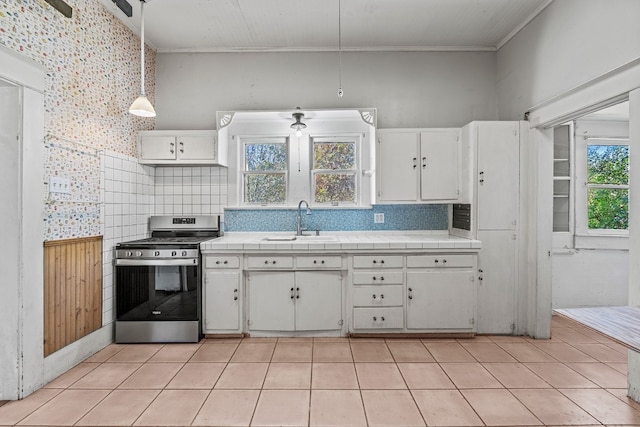 kitchen featuring sink, decorative light fixtures, tile countertops, white cabinets, and stainless steel stove