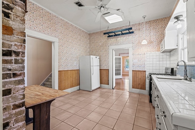 kitchen with gas stove, sink, white refrigerator, white cabinets, and tile counters