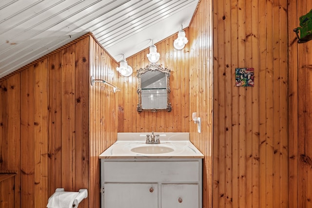 bathroom with vanity, wooden walls, and vaulted ceiling