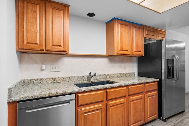 kitchen with light stone countertops, backsplash, stainless steel appliances, sink, and light hardwood / wood-style flooring