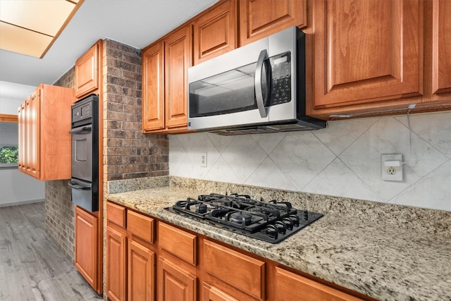 kitchen featuring light wood-type flooring, tasteful backsplash, light stone counters, and black appliances