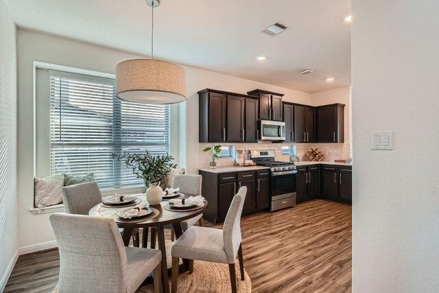 kitchen with decorative backsplash, appliances with stainless steel finishes, decorative light fixtures, and hardwood / wood-style flooring