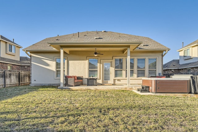 back of house with an outdoor living space, ceiling fan, a patio area, a hot tub, and a lawn