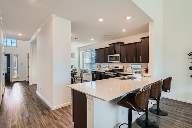 kitchen with kitchen peninsula, dark hardwood / wood-style flooring, stainless steel appliances, sink, and a breakfast bar area