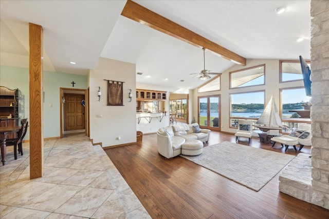 living room featuring beam ceiling, ceiling fan, light hardwood / wood-style flooring, high vaulted ceiling, and a water view