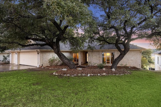 ranch-style home featuring a garage, concrete driveway, a front lawn, and stone siding