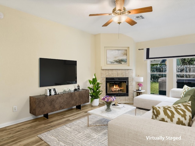 living room with light hardwood / wood-style floors, vaulted ceiling, ceiling fan, and a tiled fireplace