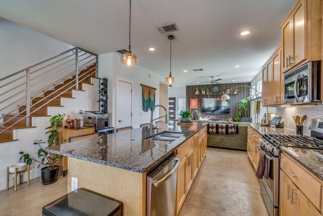 kitchen featuring ceiling fan, sink, stainless steel appliances, decorative backsplash, and a kitchen island with sink