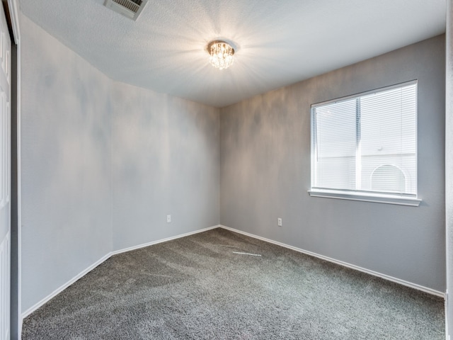 unfurnished room with baseboards, visible vents, dark carpet, and a chandelier